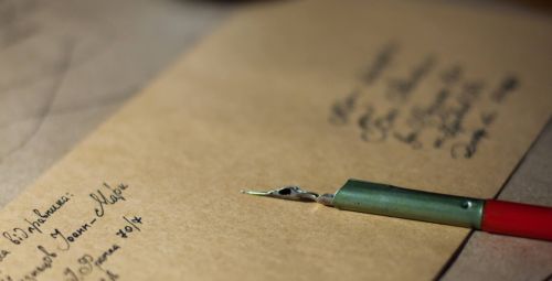 A close-up, shallow-depth-of-field shot of a vintage dip pen resting on an old, yellowish envelope.